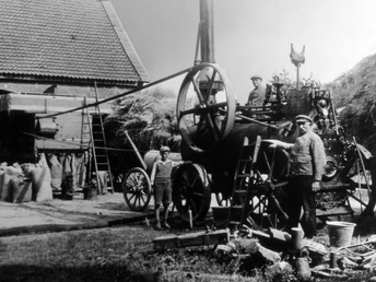 Historische landwirtschaftliche Szene: Ein Dampfdrescher verarbeitet Getreide auf einem Bauernhof.