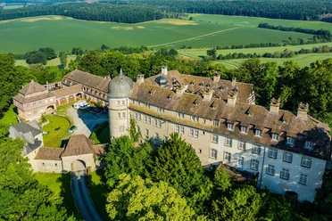Luftaufnahme der Hinnenburg, umgeben von dichten Wäldern und weiten Feldern in malerischer Umgebung.