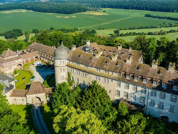 Luftaufnahme der Hinnenburg, umgeben von dichten Wäldern und weiten Feldern in malerischer Umgebung.