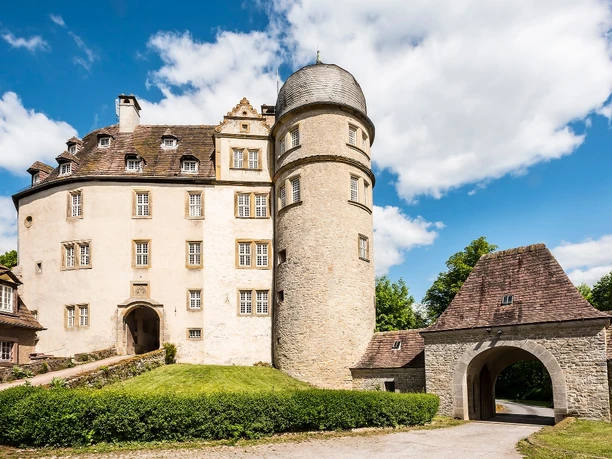 Hinnenburg Hinnenburg mit rundem Turm, historischem Gebäudekomplex und umgebenden Grünflächen unter blauem Himmel.