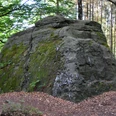 Fauler Jäger Ein großer, moosbewachsener Felsen im Wald, umgeben von Bäumen und bedeckt mit Herbstlaub.