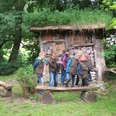 Kinder in grünen Westen erkunden ein mit Holz und Naturmaterialien gefülltes Insektenhotel im Wald.