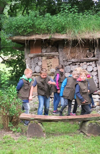 Insektenhotel am Waldhaus Durbeke bei Altenbeken Kinder in grünen Westen erkunden ein mit Holz und Naturmaterialien gefülltes Insektenhotel im Wald.
