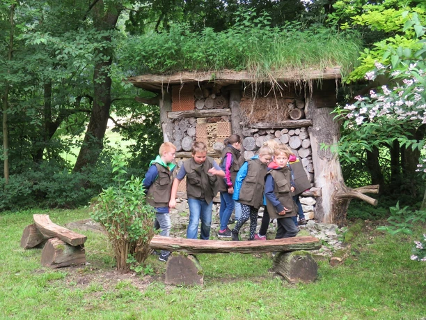 Insektenhotel am Waldhaus Durbeke bei Altenbeken Kinder in grünen Westen erkunden ein mit Holz und Naturmaterialien gefülltes Insektenhotel im Wald.