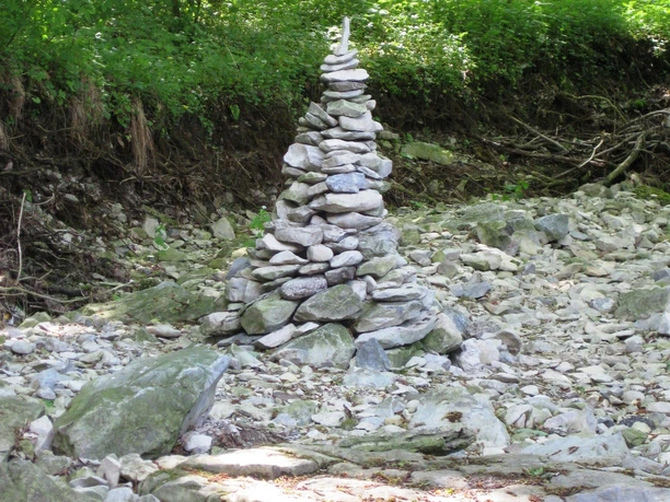 Waldzauber in der Durbeke bei Altenbeken Eine Pyramide aus gestapelten Steinen steht im trockenen Flussbett, umgeben von dichtem Wald.