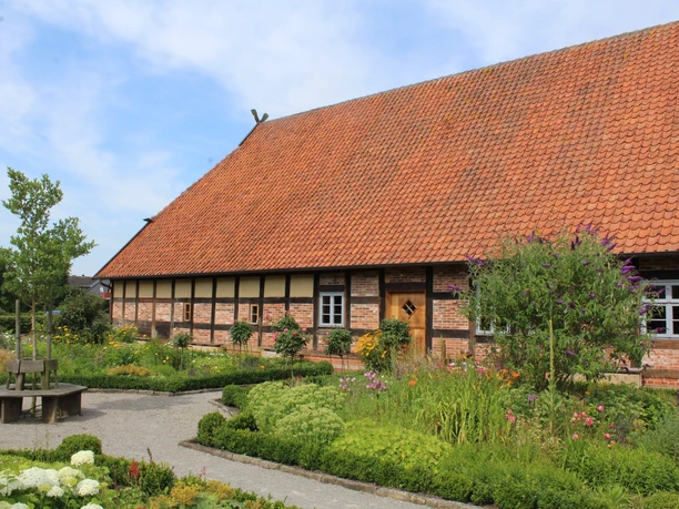 Ehmken Hoff Dörverden Backsteingebäude mit rotem Ziegeldach inmitten von Blumenbeeten und gepflegten Grünflächen.