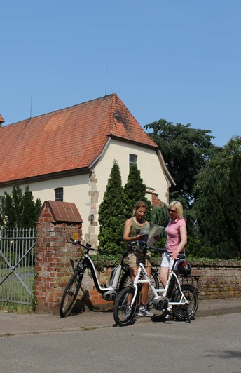 Kirche Eystrup Zwei Fahrradfahrerinnen im Gespräch vor der historischen Kirche Eystrup mit markantem Turm.
