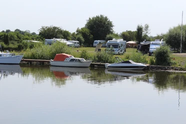 Campingplatz Drakenburg Wohnmobile und Boote am idyllischen Flussufer, umgeben von Bäumen und grünen Wiesen.