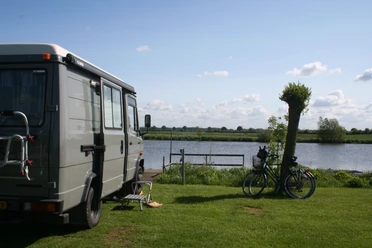 Campingplatz am See Wohnmobil steht auf einer Wiese am See, neben zwei Fahrrädern und einem Stuhl mit Blick aufs Wasser.