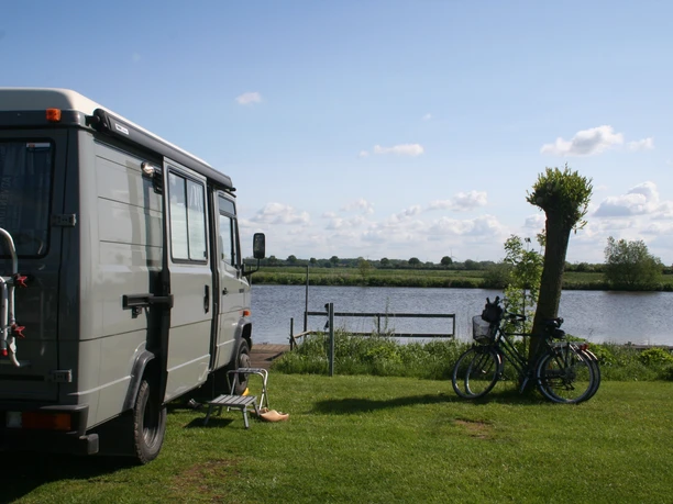 Campingplatz am See Wohnmobil steht auf einer Wiese am See, neben zwei Fahrrädern und einem Stuhl mit Blick aufs Wasser.