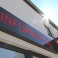 Eingang einer Tourist-Information mit rotem Schriftzug, Sonnenschein reflektiert am Gebäude.