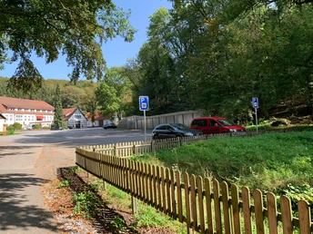 Ein Parkplatz mit mehreren geparkten Autos, umgeben von Bäumen und einem Holzzaun im Vordergrund.