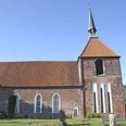 Evangelisch-reformierte Kirche in Rysum Backsteinkirche mit hohem Turm und spitzem Helm, umgeben von alten Grabsteinen unter blauem Himmel.