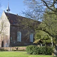 Kirche Visquard Backsteinkirche in Visquard mit rotem Ziegeldach, kleinem Turm und umgebenden Bäumen im Frühlingslicht.