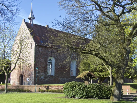 Kirche Visquard Backsteinkirche in Visquard mit rotem Ziegeldach, kleinem Turm und umgebenden Bäumen im Frühlingslicht.