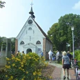 Kirche Woltzeten Weiße Backsteinkirche mit Uhrturm und Garten, Menschen mit Fahrrädern gehen zum Eingang.