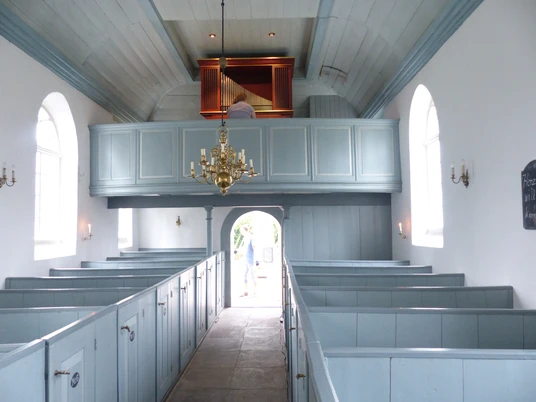 Kirche Woltzeten innen Helles Kirchenschiff mit hellblauen Holzbänken, Kronleuchter und Orgel auf der Empore.