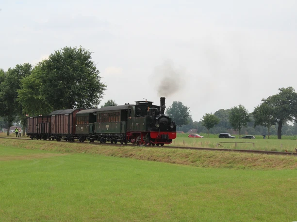 Historic steam locomotive pulls several carriages through green countryside near Bruchhausen-Vilsen.