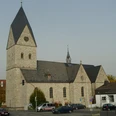 Historische Kirche mit hohem Turm, grauem Steinmauerwerk und einem Uhrziffernblatt über der Kreuzung.