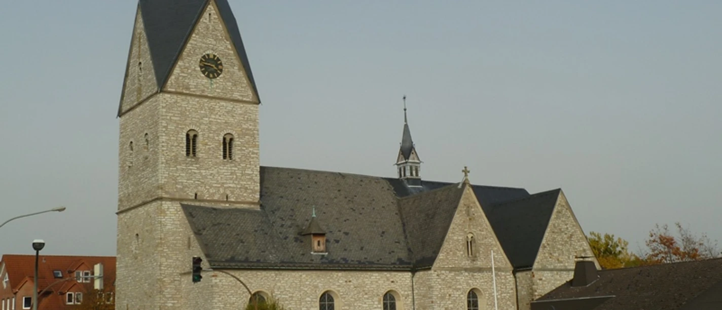 Historische Kirche mit hohem Turm, grauem Steinmauerwerk und einem Uhrziffernblatt über der Kreuzung.