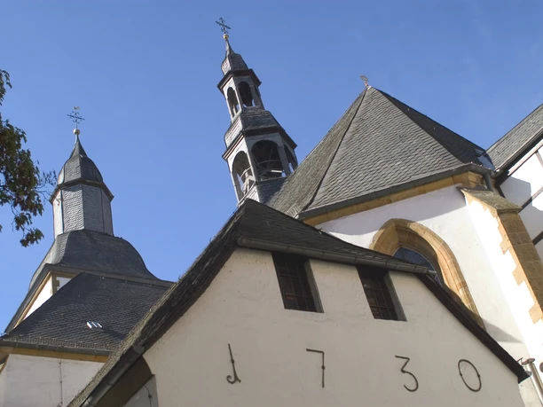 Historische Kirche mit markantem Glockenturm und blendend weißen Fassaden unter klarem Himmel.