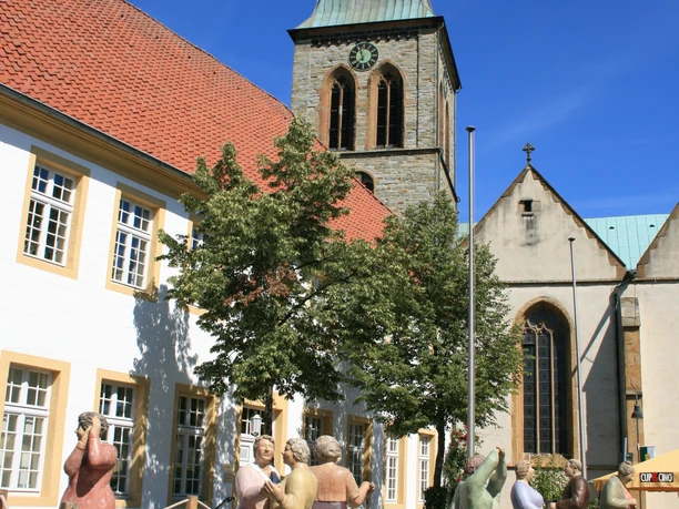 Historisches Rathaus und Aegidiuskirche am Marktplatz Wiedenbrück Figuren tanzen im Kreis auf Holzbühne vor historischer Kirche mit Turm und bunten Fenstern.