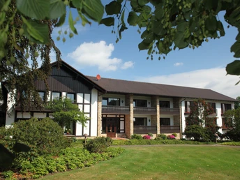 Berggasthof Wilhelmshöhe mit grüner Gartenanlage und traditioneller Architektur vor blauem Himmel.
