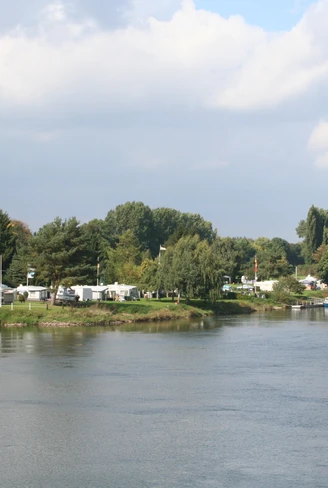 Am Flussufer des Weserflusses gelegener Campingplatz, umgeben von grüner Natur und Bäumen.