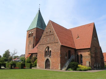 Backsteinkirche mit rotem Satteldach und markantem Turm vor klarem blauem Himmel in Riede.