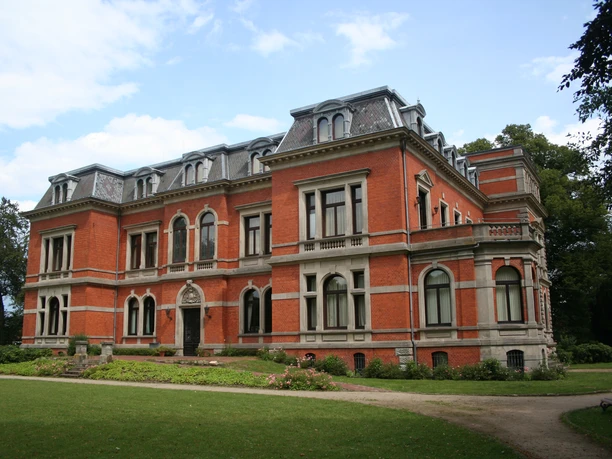 Schloss Etelsen Backsteinfassade des Schloss Etelsen mit grauen Akzenten, umgeben von gepflegten Grünanlagen.