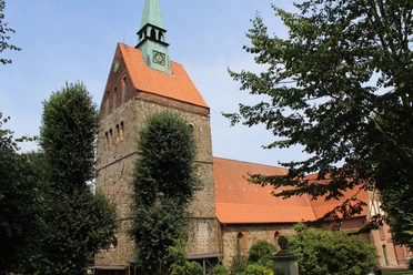 Brick church with green tower, embedded in lush greenery; architectural heritage.