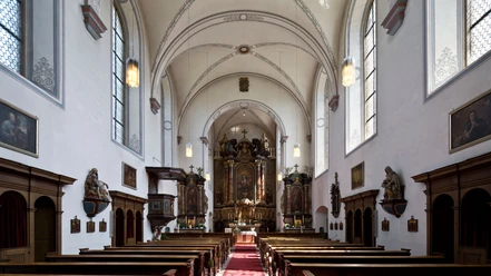 Helle Innenansicht der Kapuzinerkirche mit einem reich verzierten Altar und knienden Holzbänken.