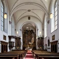 Helle Innenansicht der Kapuzinerkirche mit einem reich verzierten Altar und knienden Holzbänken.