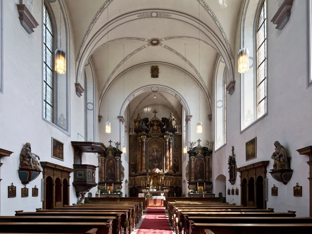 Helle Innenansicht der Kapuzinerkirche mit einem reich verzierten Altar und knienden Holzbänken.