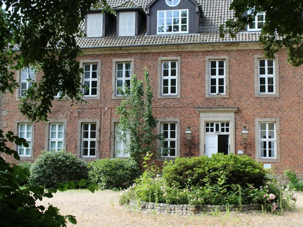 Red brick building with several mullioned windows and green entrance area in Bruchhausen-Vilsen.