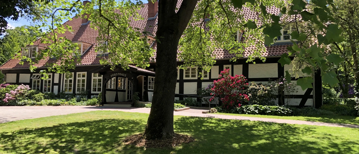 A half-timbered house surrounded by a lush, green lawn, a large tree provides shade in the foreground.