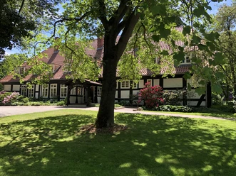 Forsthaus Heiligenberg Bruchhausen-Vilsen Ein Fachwerkhaus umgeben von üppigem, grünem Rasen, ein großer Baum bietet Schatten im Vordergrund.