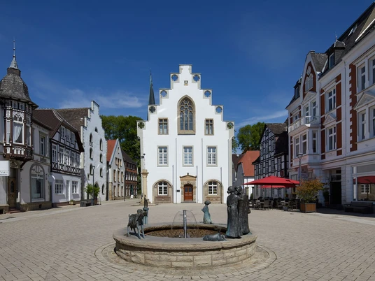 Rathaus von Brakel mit Giebel-Spitzdach, umgeben von historischen Gebäuden, zentraler Brunnen.