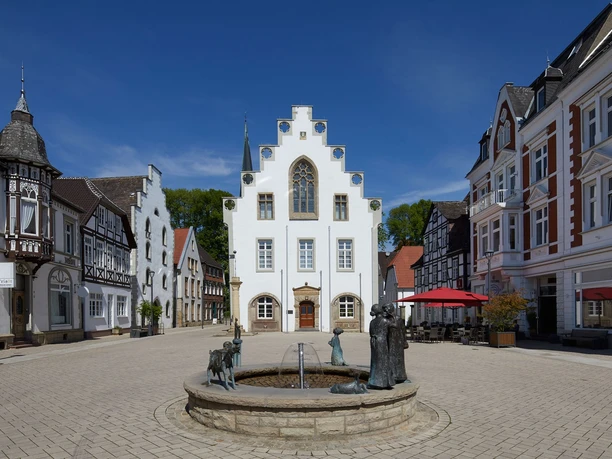 Rathaus von Brakel mit Giebel-Spitzdach, umgeben von historischen Gebäuden, zentraler Brunnen.