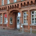 Rotes Backsteingebäude mit hohen Fenstern und Eingang zur Tourist-Information Nienburg an der Straße.Red brick building with high windows and entrance to the Nienburg Tourist Information Office on the street.Rød murstensbygning med høje vinduer og indgang til Nienburg Tourist Information Centre på gaden.Gebouw van rode baksteen met hoge ramen en ingang van het Nienburg Tourist Information Centre aan de straat.