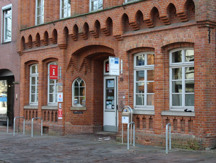 Rotes Backsteingebäude mit hohen Fenstern und Eingang zur Tourist-Information Nienburg an der Straße.Red brick building with high windows and entrance to the Nienburg Tourist Information Office on the street.Rød murstensbygning med høje vinduer og indgang til Nienburg Tourist Information Centre på gaden.Gebouw van rode baksteen met hoge ramen en ingang van het Nienburg Tourist Information Centre aan de straat.