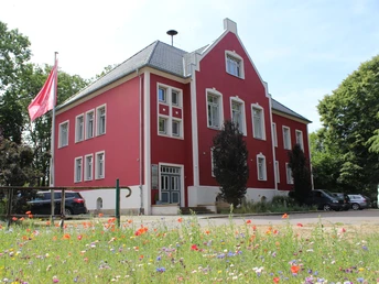 Amtshof 1 Bruchhausen-Vilsen Ein rotes, historisches Gebäude in Bruchhausen-Vilsen, umgeben von Blumenwiese und Parkplätzen.