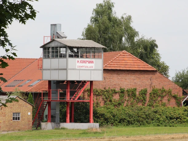 Kartoffeldämpfanlage Stöckse Alte Kartoffeldämpfanlage H. Kuhlmann mit rotem Dach, umgeben von ländlicher Vegetation in Stöckse.