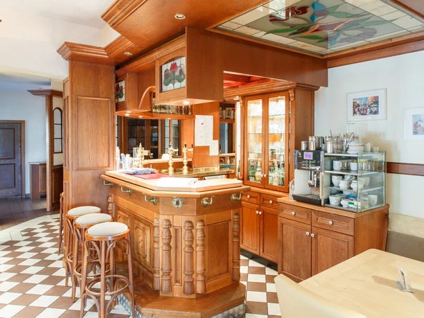 Gaststätte Timmer Theke_KHB_8782.jpg Holztheke mit drei Barhockern, Gläserregal und Kaffeemaschine in einem hellen Gastraum.