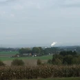 Blick nach Lage Panorama über eine weite, flache Landschaft mit Feldern und Bauernhöfen im Vordergrund, Hügeln in der Ferne.