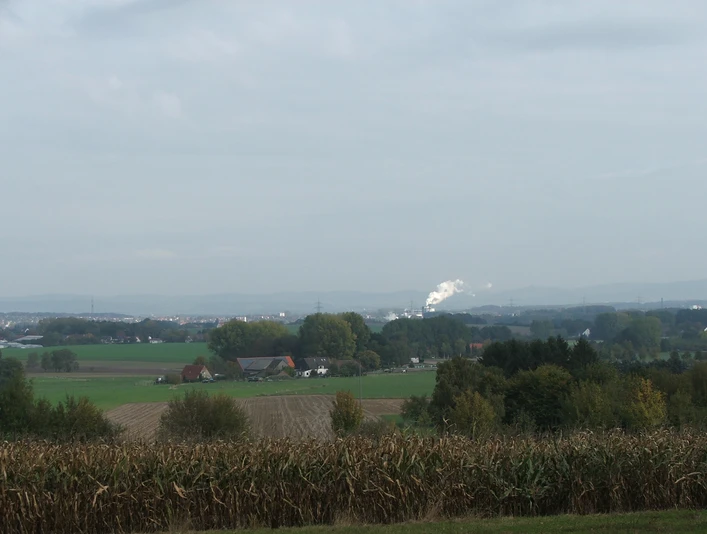 Blick nach Lage Panorama über eine weite, flache Landschaft mit Feldern und Bauernhöfen im Vordergrund, Hügeln in der Ferne.