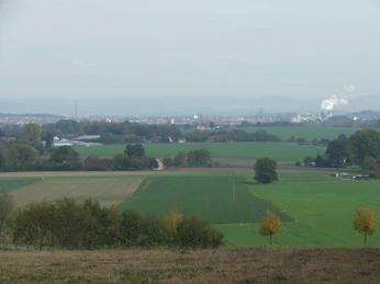 Blick nach Lage Weitläufige Wiesen und Felder mit einer Stadt im Hintergrund, umgeben von sanften Hügeln.