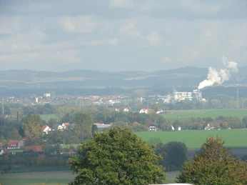 Blick nach Lage Ausblick auf eine hügelige Landschaft mit Feldern, Bäumen und rauchendem Schornstein in der Ferne.