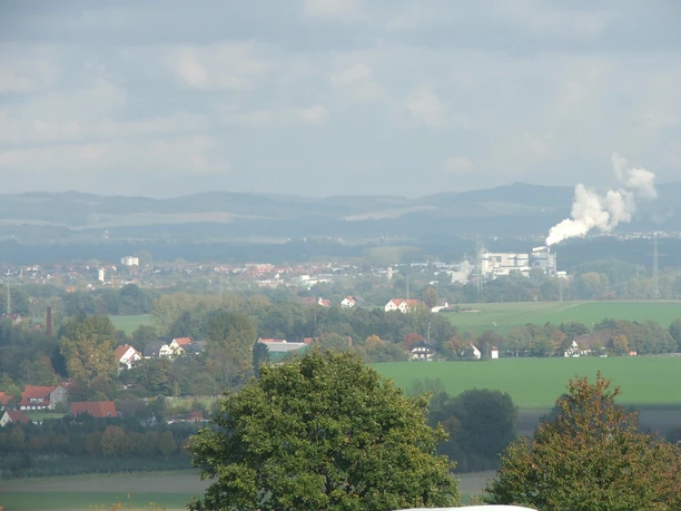 Blick nach Lage Ausblick auf eine hügelige Landschaft mit Feldern, Bäumen und rauchendem Schornstein in der Ferne.