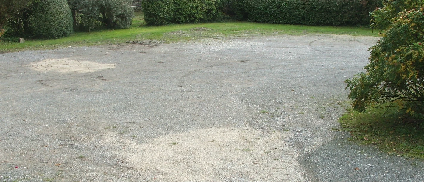 Kleiner Schotterparkplatz umgeben von dichter Vegetation, im Hintergrund dichte grüne Hecken.